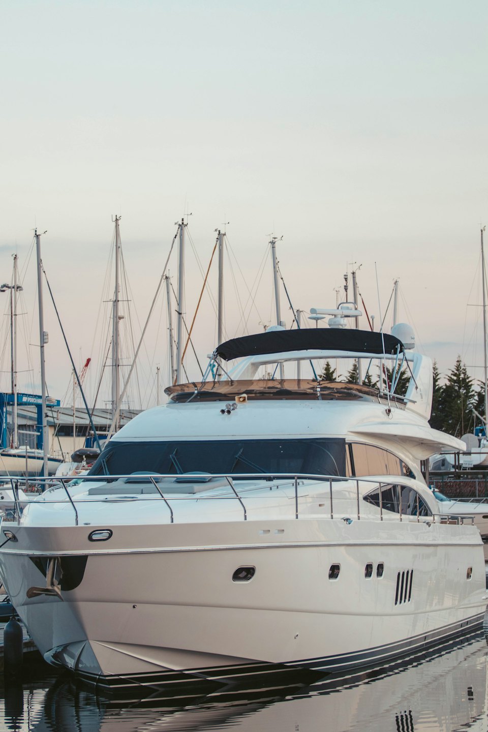 Yacht di lusso bianco ormeggiato in un porto turistico affollato al tramonto.