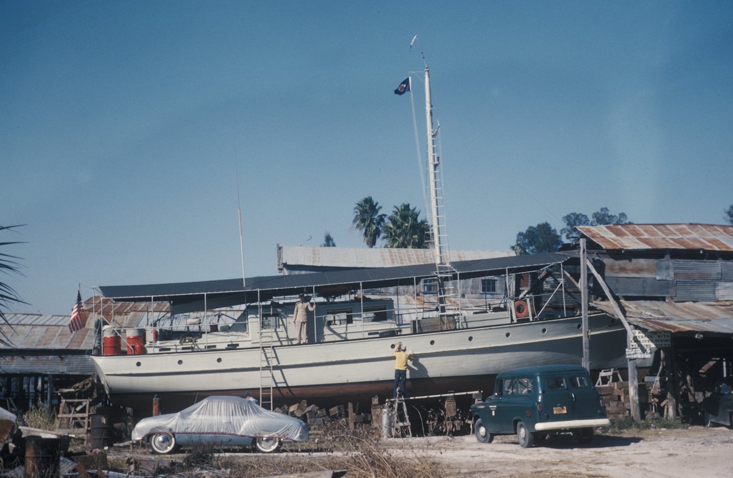 Operai riparano uno yacht d'epoca in un affollato cantiere navale.